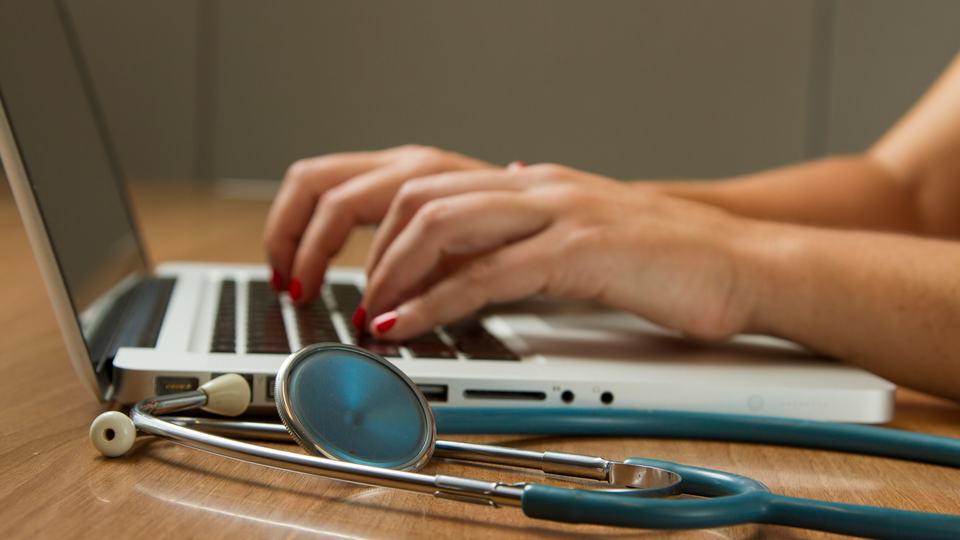 Woman's hands typing next to stethoscope