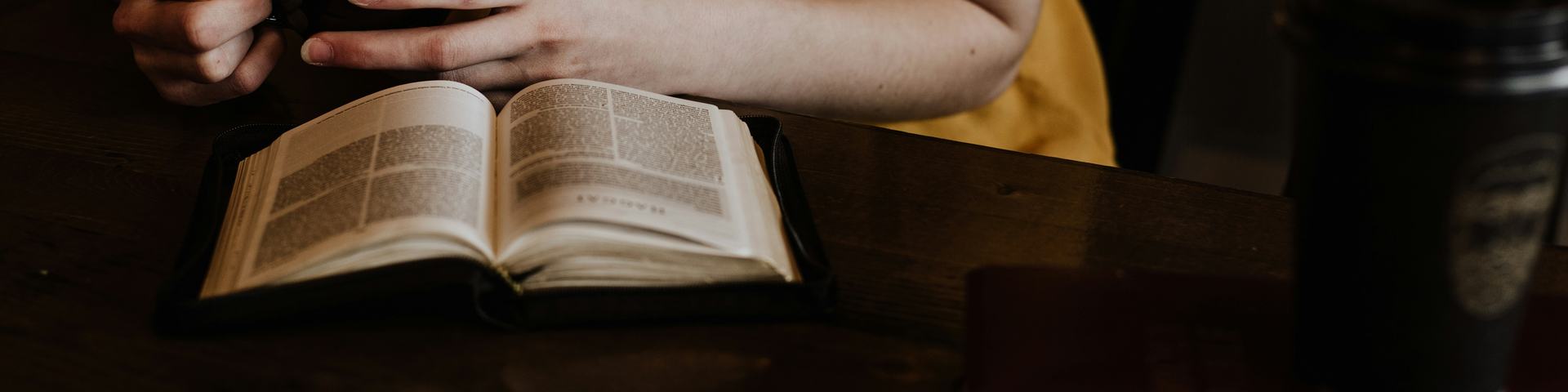 Woman holding coffee while reading Bible