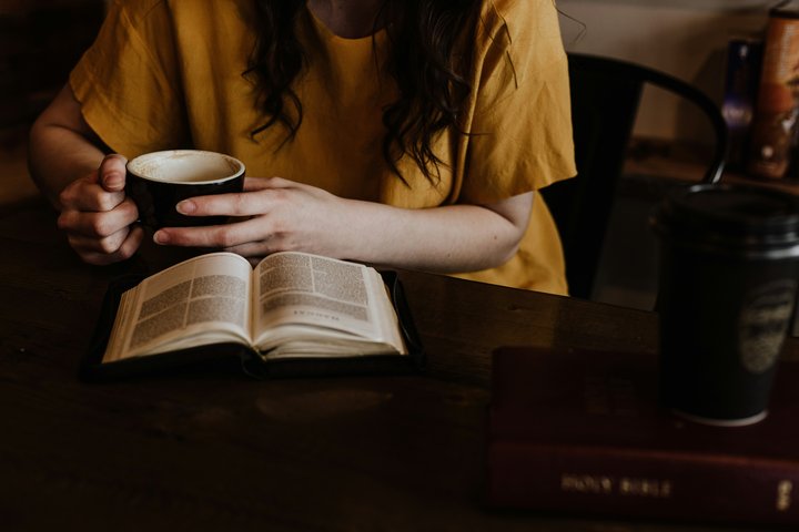 Woman holding coffee while reading Bible